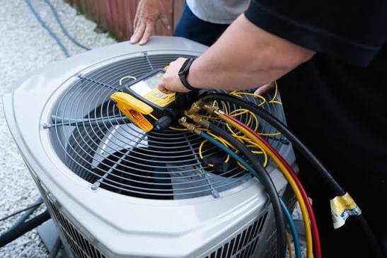 Technician connecting diagnostic hoses to an outdoor heat pump