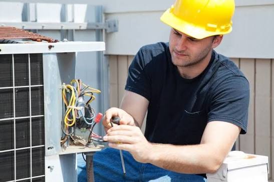 Technician examining wiring inside an outdoor HVAC condenser