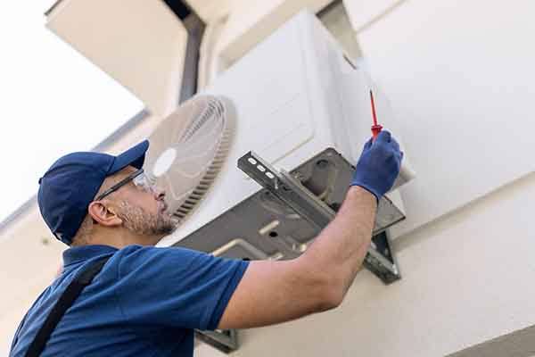 Technician working beneath a wall-mounted outdoor air conditioning unit